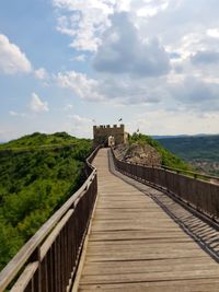 Footbridge against cloudy sky