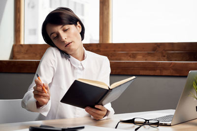 Mid adult woman using phone while sitting on table