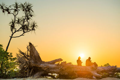 People sitting on rock against sky during sunset