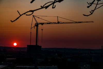 Silhouette cranes at construction site during sunset