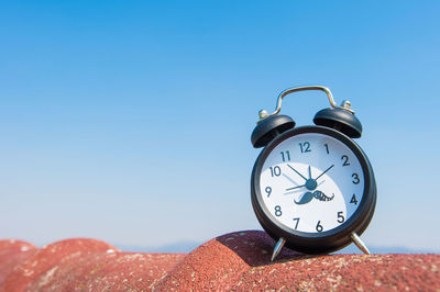 Low angle view of alarm clock against clear blue sky