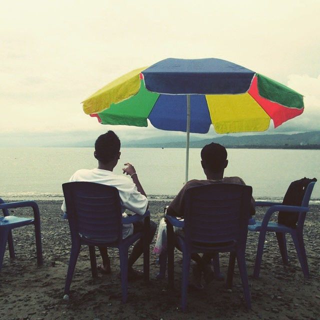 chair, sea, beach, relaxation, sitting, horizon over water, men, leisure activity, lifestyles, rear view, person, vacations, sand, water, sky, bench, absence, seat, shore