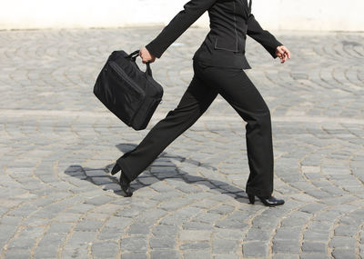 Low section of businesswoman holding bag while walking on city street