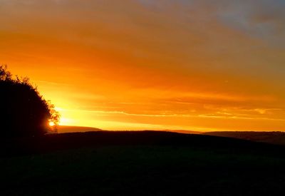 Scenic view of silhouette field against orange sky