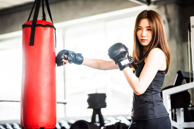 Side view of confident young woman practicing boxing with punching bag in gym