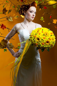 Portrait of beautiful bride holding bouquet while standing against orange background