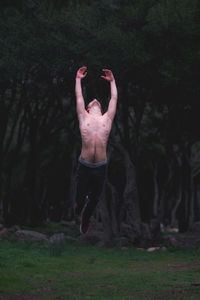 Shirtless man jumping against trees at forest