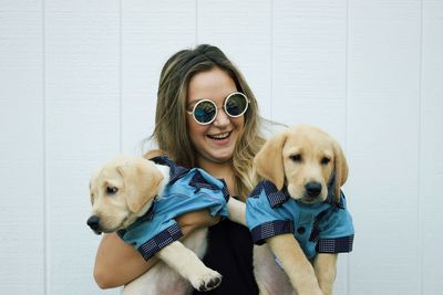 Smiling woman in sunglasses holding dogs against white wall