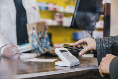 Hand of customer with mobile phone at checkout counter in chemist shop