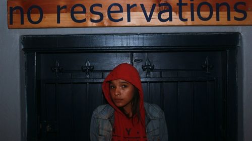 Portrait of scared woman against closed door with text on wall