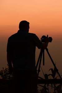 Rear view of silhouette man photographing against sky during sunset