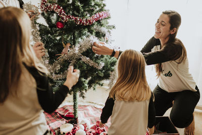 Cheerful parents with daughters decorating christmas tree at home
