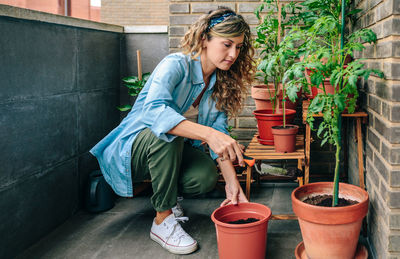 Woman using shovel to fill with soil a pot of plant in urban garden on terrace