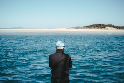Rear view of man standing by sea against sky