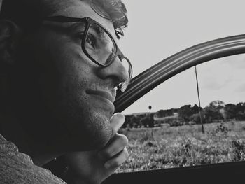 Close-up of thoughtful young man by car against sky