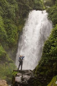Woman standing on rock by waterfall in forest