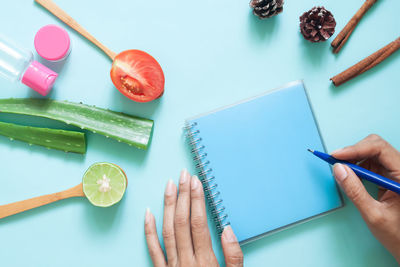 Cropped hand of woman holding pen over book by personal accessories over colored background