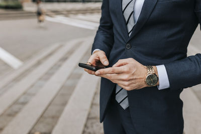 Midsection of businessman using smart phone standing at street