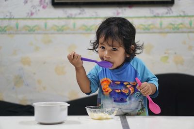 Cute baby girl eating ice cream on table at home 