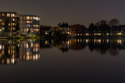 Illuminated buildings reflecting in river against sky at night