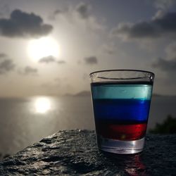 Close-up of beer in sea against sky during sunset