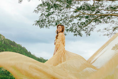 Woman standing by tree against sky