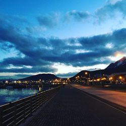 Road passing through city against cloudy sky