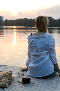 Rear view of woman standing by lake during sunset