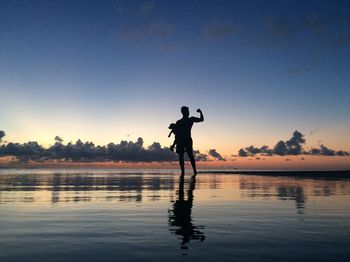 Silhouette father flexing muscles while carrying child at beach during sunset