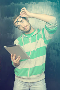 Portrait of young man using digital tablet while standing against old wall