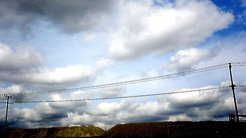 Low angle view of power lines against cloudy sky