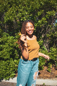 Portrait of smiling young woman standing against plants