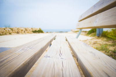 Close-up of wooden bench on beach against clear sky