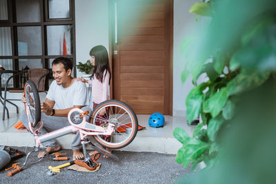 Smiling father repairing bicycle with daughter at home