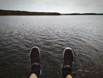 Low section of person standing by lake against sky