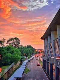 Road amidst trees and buildings against sky during sunset