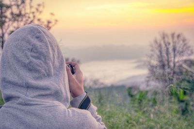 Portrait of man holding sunglasses against sky during sunset