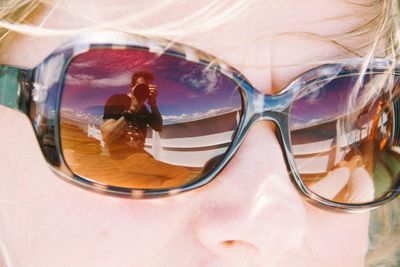 Reflection of man photographing on sunglasses of woman