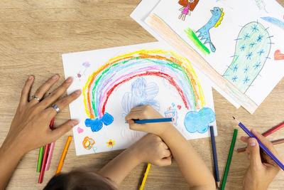Top view shot of mother and daughter are drawing and coloring beautiful rainbow picture on paper