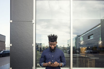 Happy man listening to music from mobile phone against window