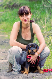 Full length portrait of woman crouching with rottweiler puppy on footpath