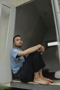 Full length of man sitting by window at home