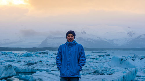 Portrait of man standing by frozen sea during sunset