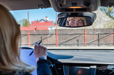 Middle-aged woman in glasses in the car working with documents and talking on the phone, rear view