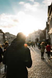 Rear view of man walking on street in city against sky