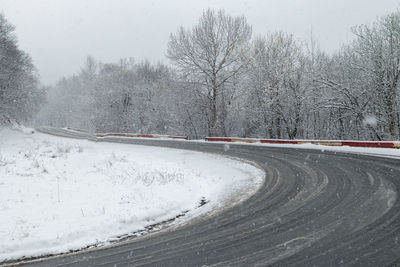 Snow covered road by trees against sky during winter