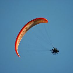 Low angle view of people paragliding against clear blue sky