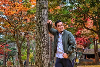 Smiling man standing by tree in park during autumn