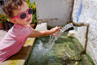 Cute girl wearing sunglasses drinking water at fountain