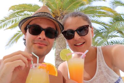 Portrait of smiling friends in sunglasses having juice against palm tree